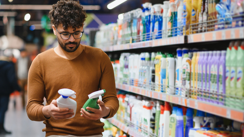 A man considers multiple cleaning products in a store aisle.
