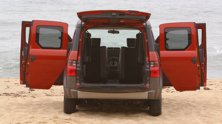 A rear perspective of an orange Honda Element parked on a sandy beach with all doors open.