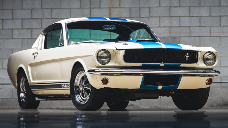 A white 1965 Shelby GT350 with signature blue Le Mans stripes parked in a professional workshop.