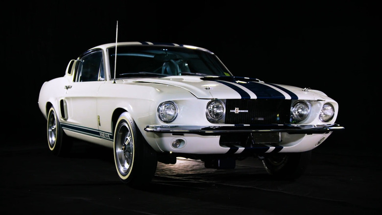 A studio shot of a white 1967 Shelby GT500 Super Snake with blue stripes against a black background.