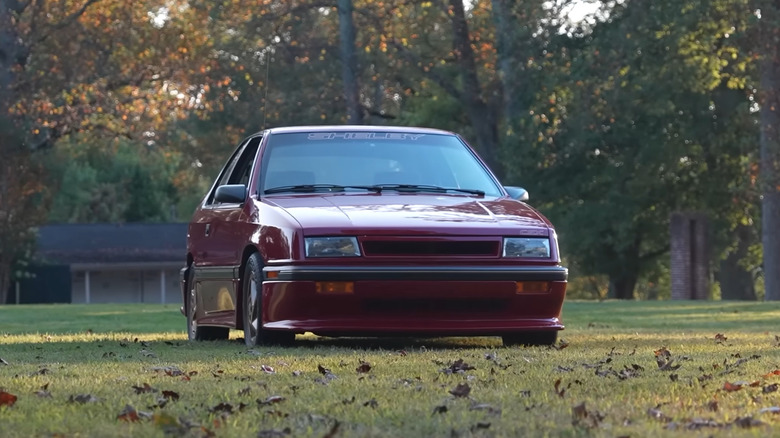 An exotic red 1989 Dodge Shelby CSX-VNT parked on a grassy field at sunset.