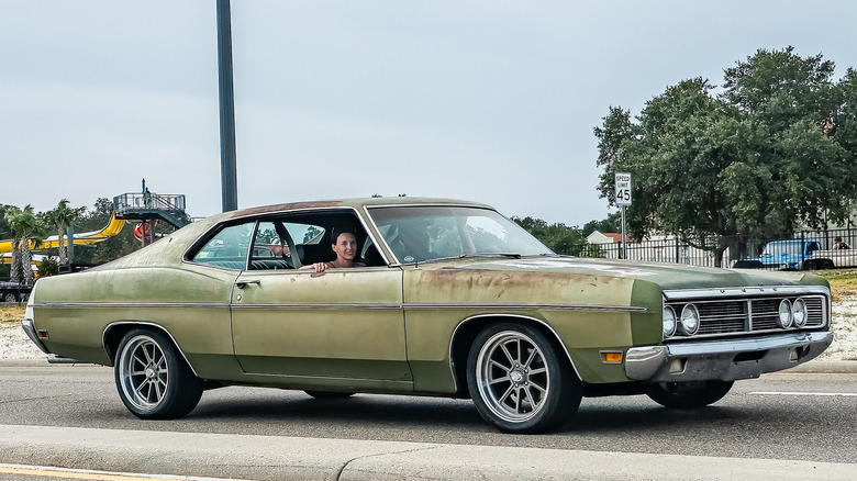 Green Ford Galaxie two-door with patina on the road