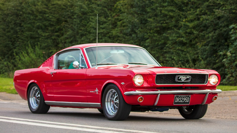 Red Ford Mustang driving on the road with trees in the background