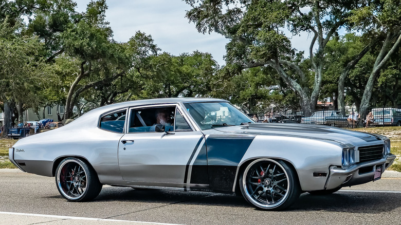 Modified Buick Skylark in silver driving near a car show