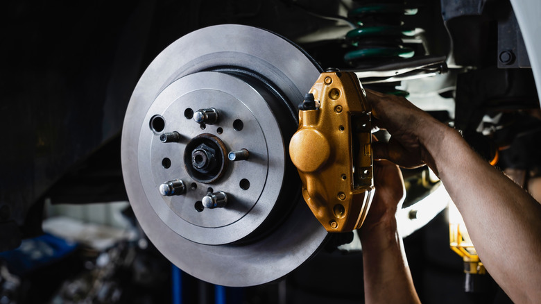 An auto mechanic works on exposed brake rotors and calipers.
