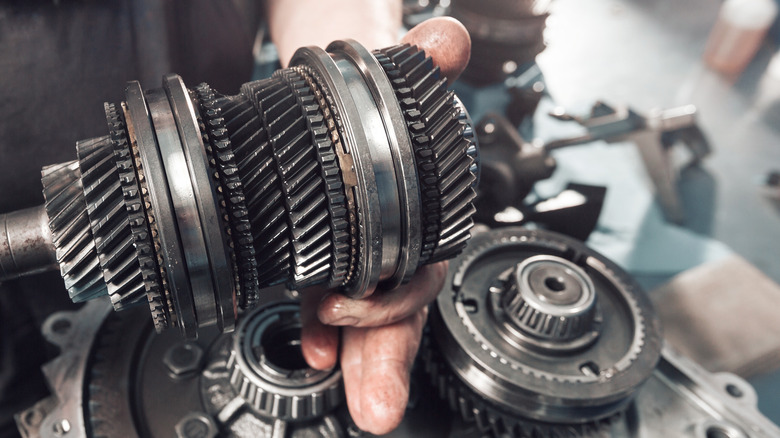 Mechanic holds disassembled transmission gears.