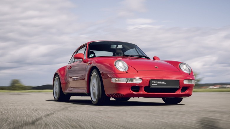 A bright red Porsche 993-generation 911 coupe captured in motion on a track, featuring the classic air-cooled body silhouette.