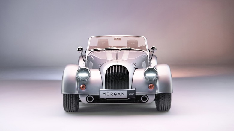 A sleek, dark grey Morgan Plus Six convertible parked in a studio setting, highlighting its classic, hand-crafted aesthetic and wire-spoke wheels.