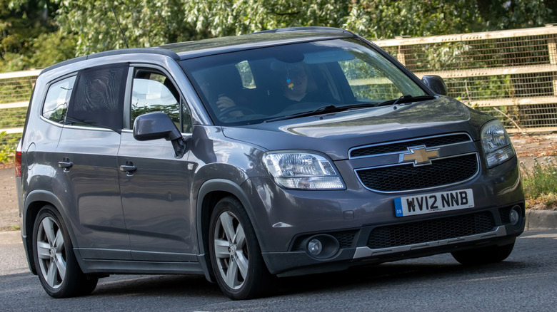 A grey Chevy Orlando is traveling down a road.