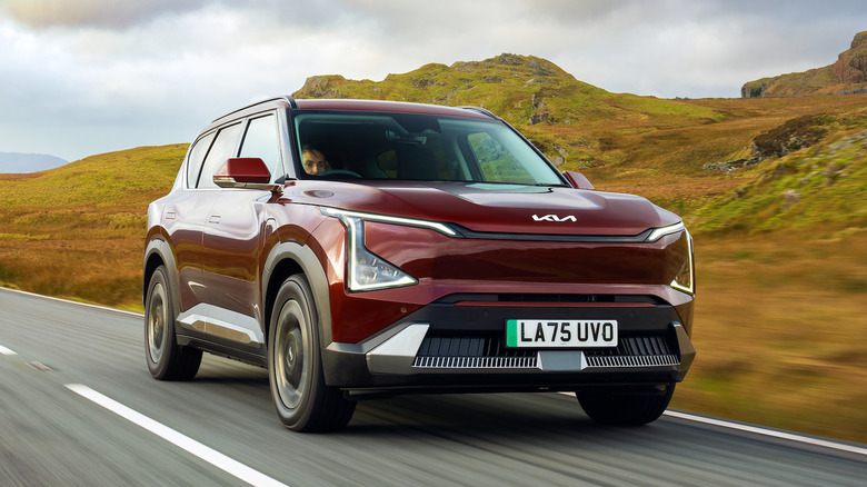 A red Kia EV5 drives on an open road.