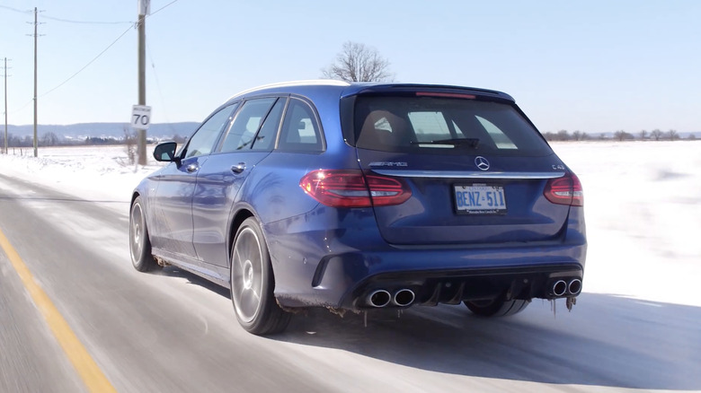 A blue Mercedes-AMG C43 Wagon drives through light snow.