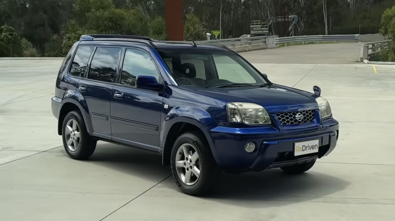 A blue Nissan X-Trail sits in a parking lot.