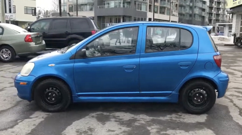 A blue Toyota Echo Hatchback parked in a city.