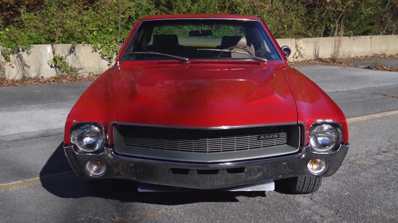 A red AMC AMX parked in an overgrown parking lot.