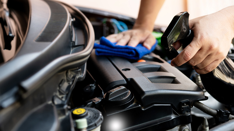 Man with spray cleaner and towel cleaning engine cover.
