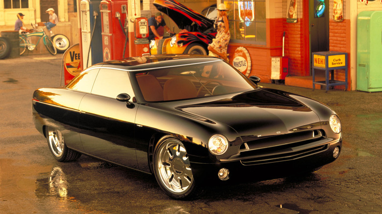 The gloss black 2001 Ford Forty-Nine concept coupe parked in front of a retro 1950s-style service station, highlighting its sleek slab-sided body, round headlights, wide horizontal grille, and large polished wheels.