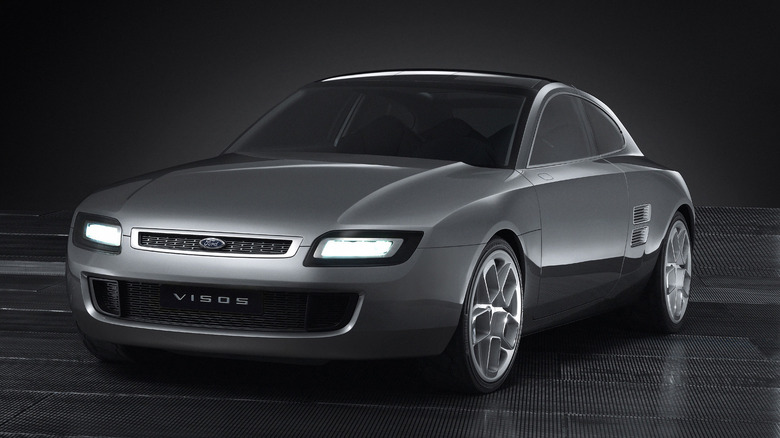 The metallic silver 2003 Ford Visos concept coupe, highlighting its Capri-inspired fastback silhouette, slim upper grille with illuminated rectangular headlights, rear-fender louvers, and sculpted multi-spoke alloy wheels against a dark background.