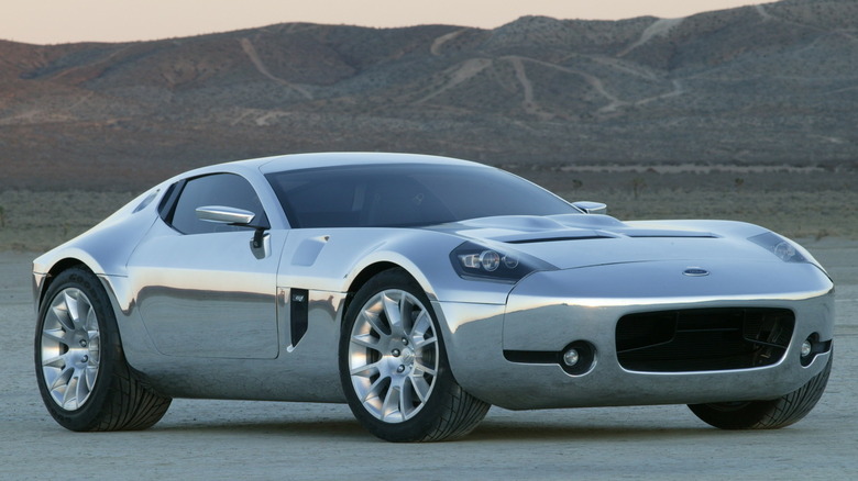The 2004 Ford Shelby GR-1 concept coupe in full mirror-finish bare aluminum, showcasing its long sculpted hood, prominent grille intake, and Kamm-tail profile, on an open desert flat.