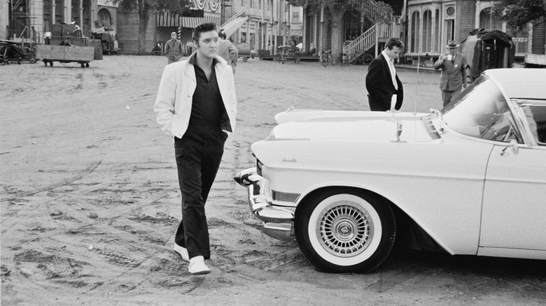 Elvis Presley walking past a Cadillac