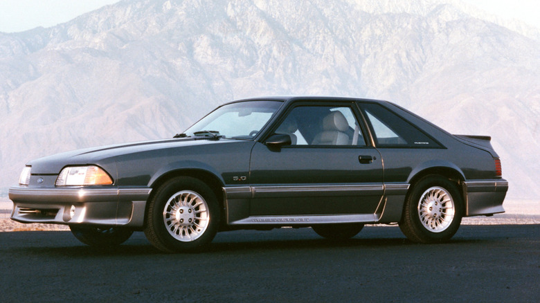 1989 Ford Mustang sits in front of mountainous background.