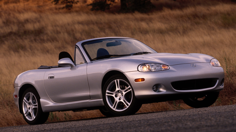 Silver NB Mazda Miata set among grassy hills.