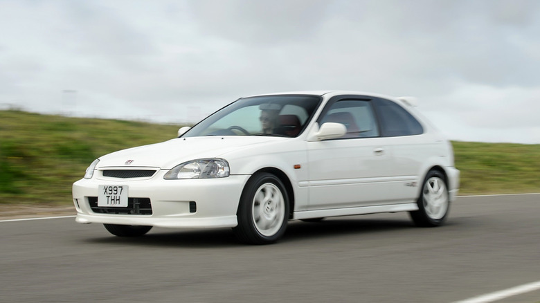 A Championship White Honda Civic Type R (EK9) three-door hatchback in motion on an open track, showing its matching white alloy wheels, subtle chin spoiler, and factory roof wing.