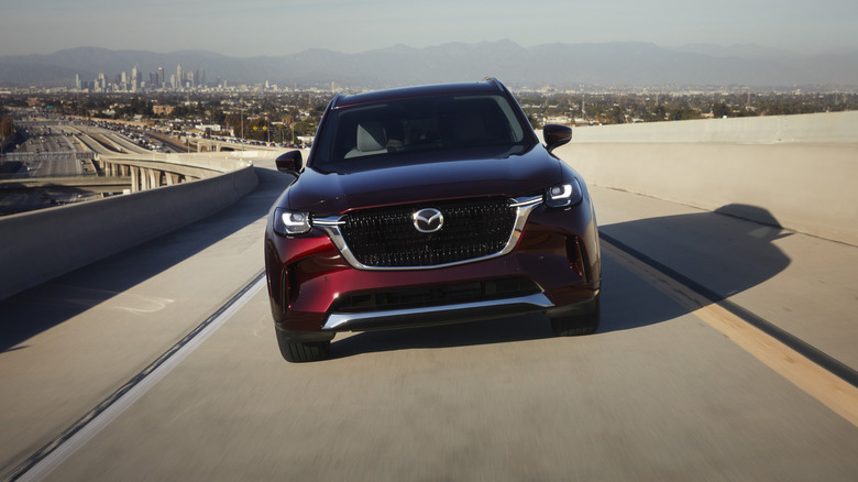 A red Mazda CX-90 is shot driving from the front.