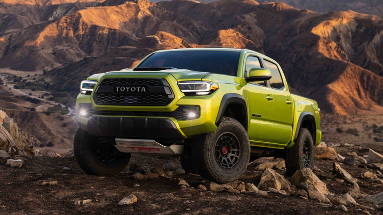 A yellow Toyota Tacoma driving across rocky terrain off-road with its fog lights shining.