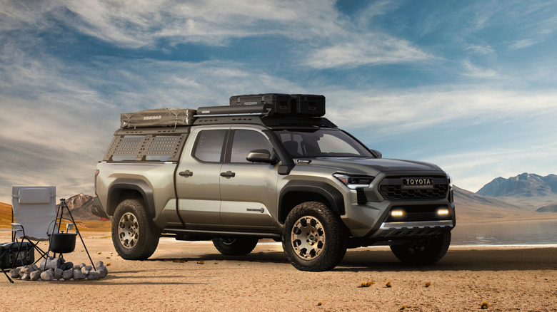 An off-road equipped Toyota Tacoma parked on dirt with a fire pit and a chair next to it.