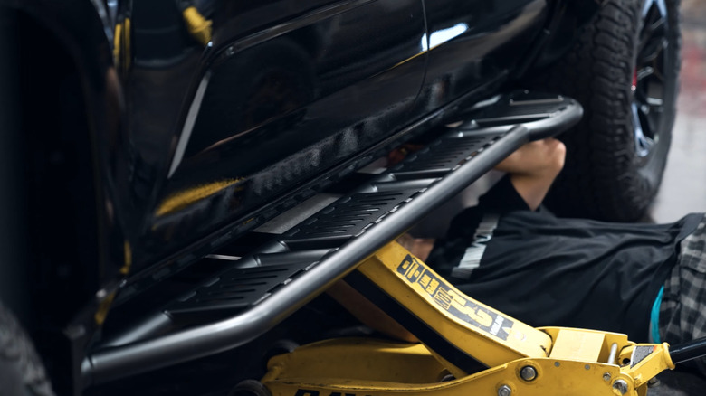 A man under a Toyota Tacoma in the process of having rock sliders installed.