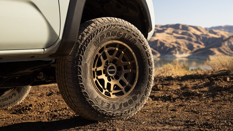 A close-up of a front right all-terrain tire on a Toyota Tacoma parked in dirt.