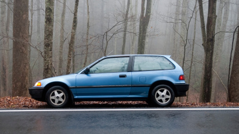 A blue Honda Civic is parked along the road in foggy woods.