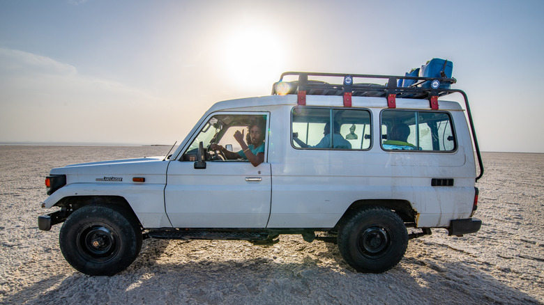 A white Toyota Land Cruiser passes through a desert.