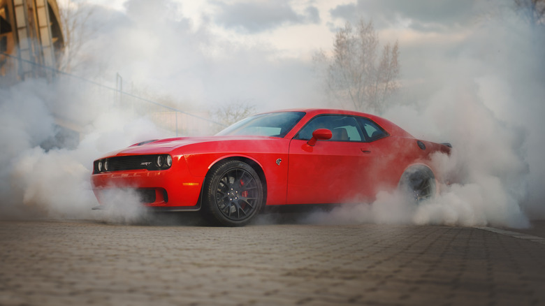 A red Dodge Challenger Hellcat doing a burnout on a cobblestone surface.