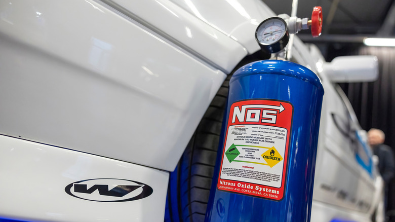 This is a blue nitrous oxide bottle sitting outside of a white vehicle.