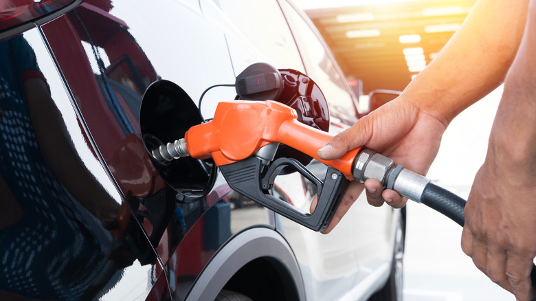 This is a person pumping fuel from an orange pump handle into a black vehicle.