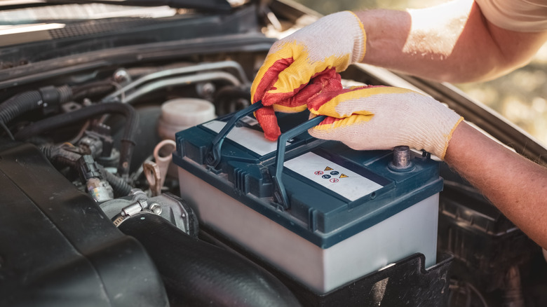 Mechanic lifting new battery into engine bay.