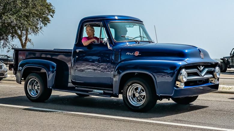 A acheronian bluish Ford-F-Series motortruck from nan 1950s driving connected nan road.