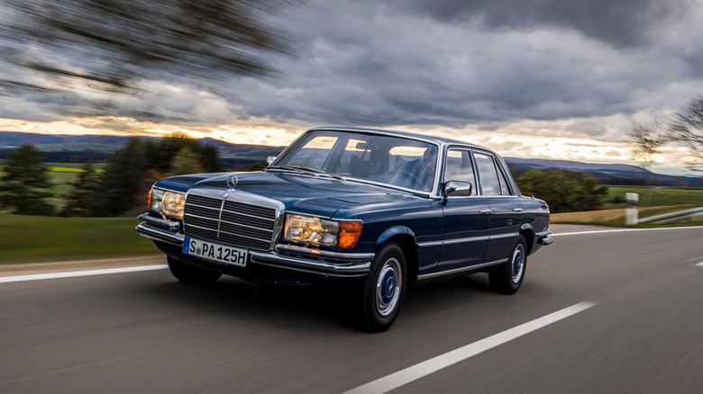 A 1970s blue Mercedes-Benz S-Class driving on a road.