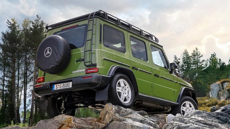 A green G-Class sits on rocks with tall trees in the background