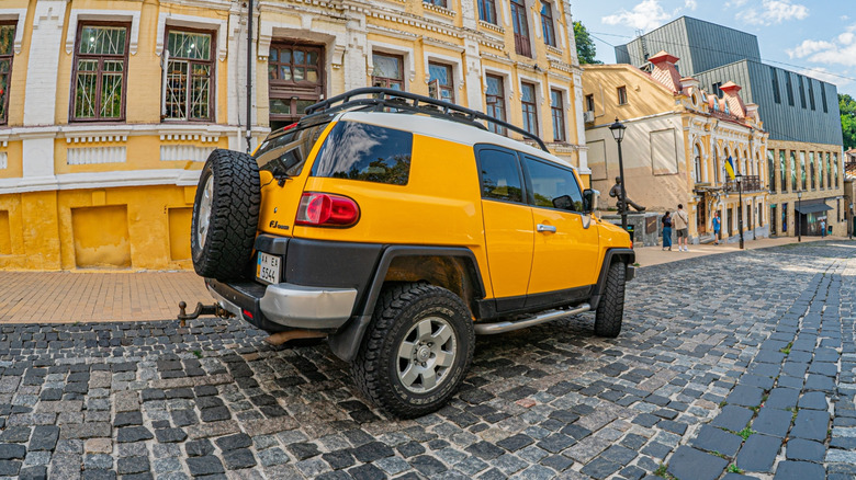 A yellow Toyota FJ Cruiser on a sloped cobblestone street in front of antique buildings