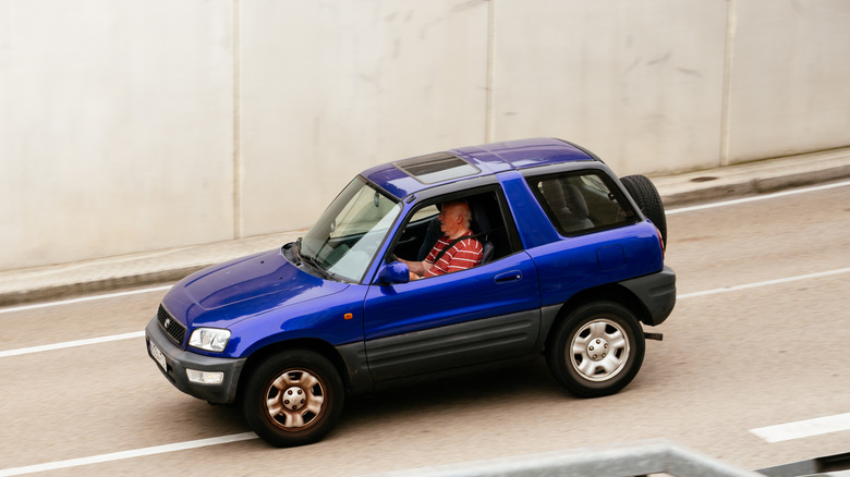 A purple Toyota RAV4 is photographed from above while driving on a highway next to a wall.