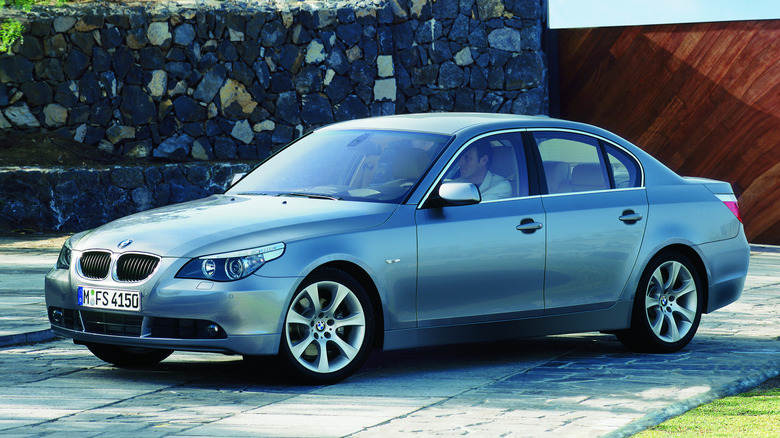 A silver E60-generation BMW 5 Series sedan parked on a stone-paved driveway, captured from a front-three-quarter perspective.