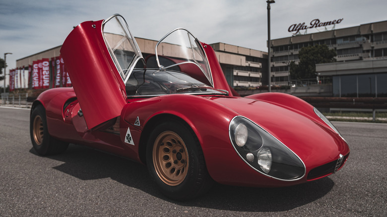 A low-angle front-three-quarter view of a classic red Alfa Romeo 33 Stradale parked on an asphalt track.
