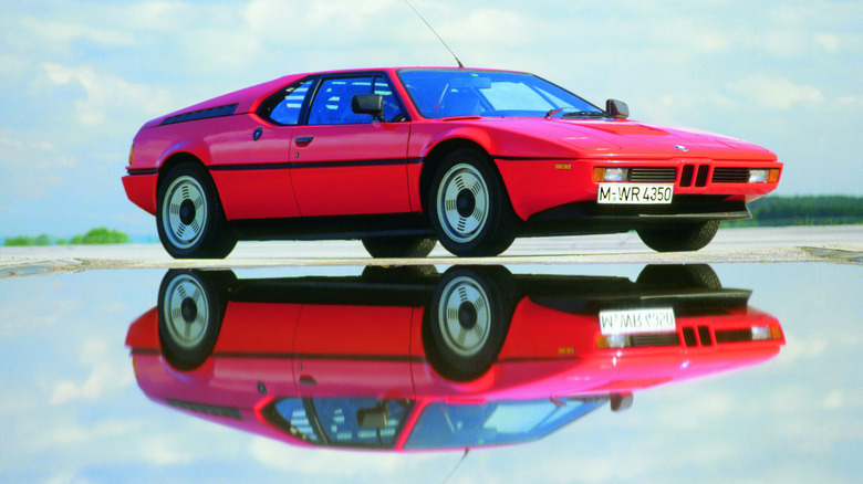 A low-angle studio photograph of a bright red 1979 BMW M1 supercar parked on a wet surface.