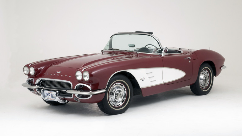 Front 3/4 studio shot of a dark red 1961 Chevrolet Corvette C1 convertible on white background.