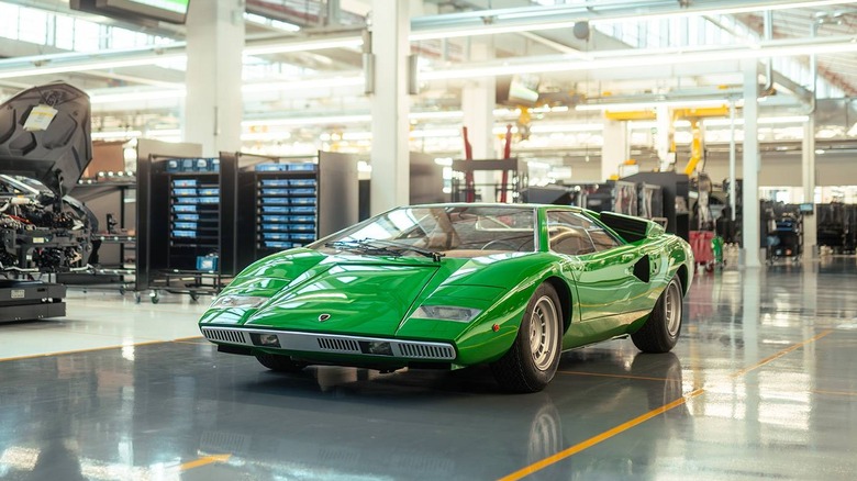 A studio photograph of a classic bright green Lamborghini Countach LP400 prototype positioned at a front-three-quarter angle against a seamless, solid white background.