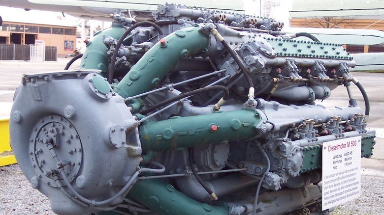 A close-up, outdoor view of a Soviet Zvezda M503 liquid-cooled radial engine on a gravel display with its dense, complex cluster of 42 cylinders.