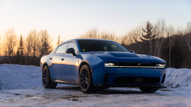 Front three-quarter view of a blue Dodge Charger Daytona EV parked on a snowy road at sunset.