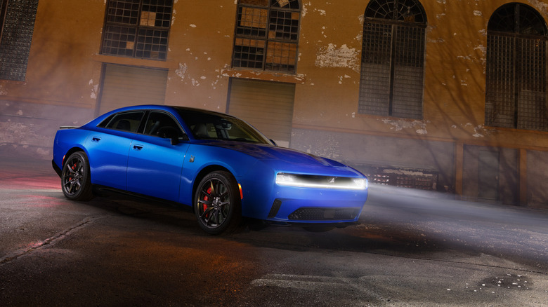 Blue Dodge Charger Daytona EV parked at night with illuminated front light bar in front of an industrial brick building.